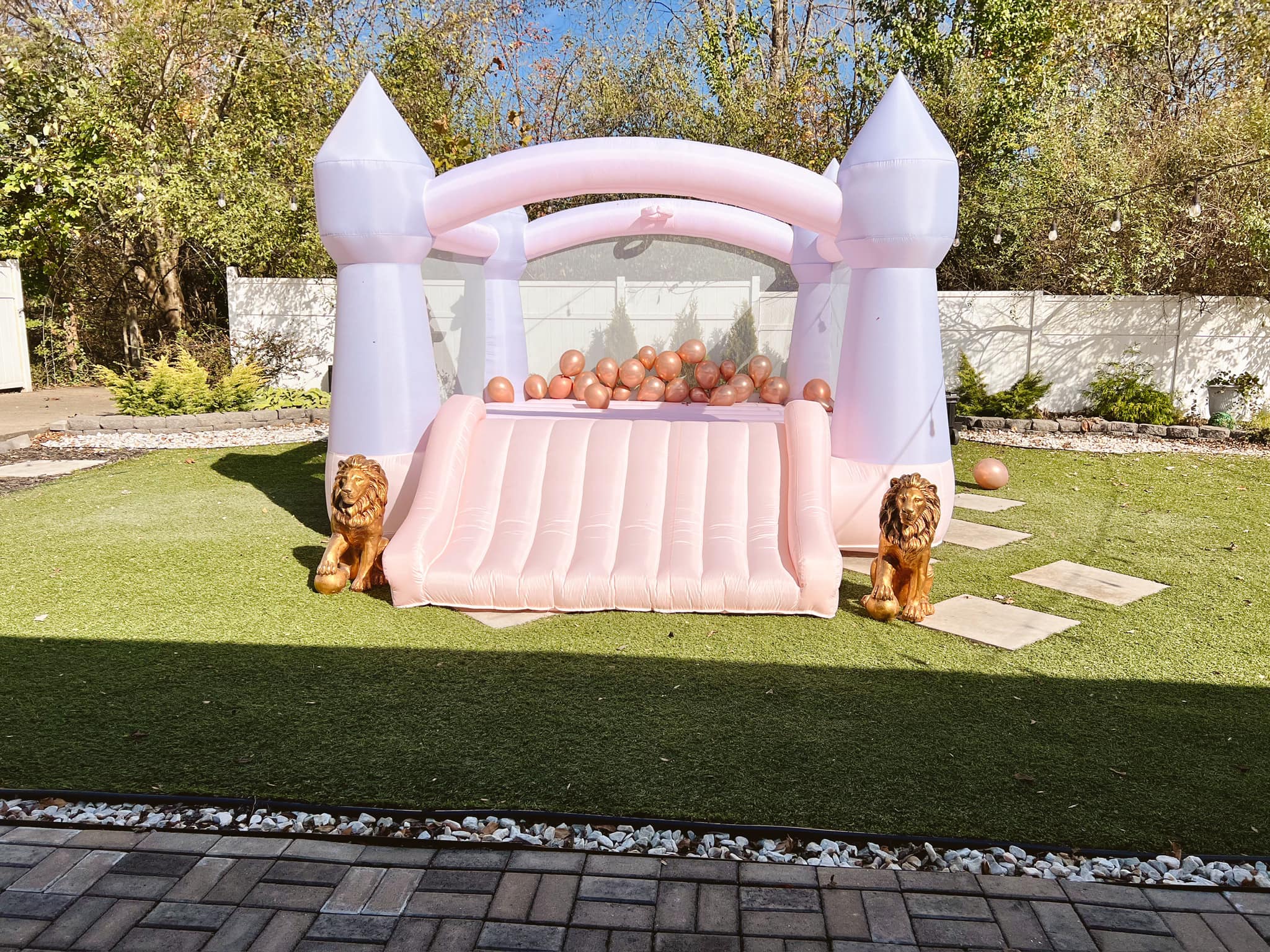 Pink and white castle bounce house with gold lions on a green lawn