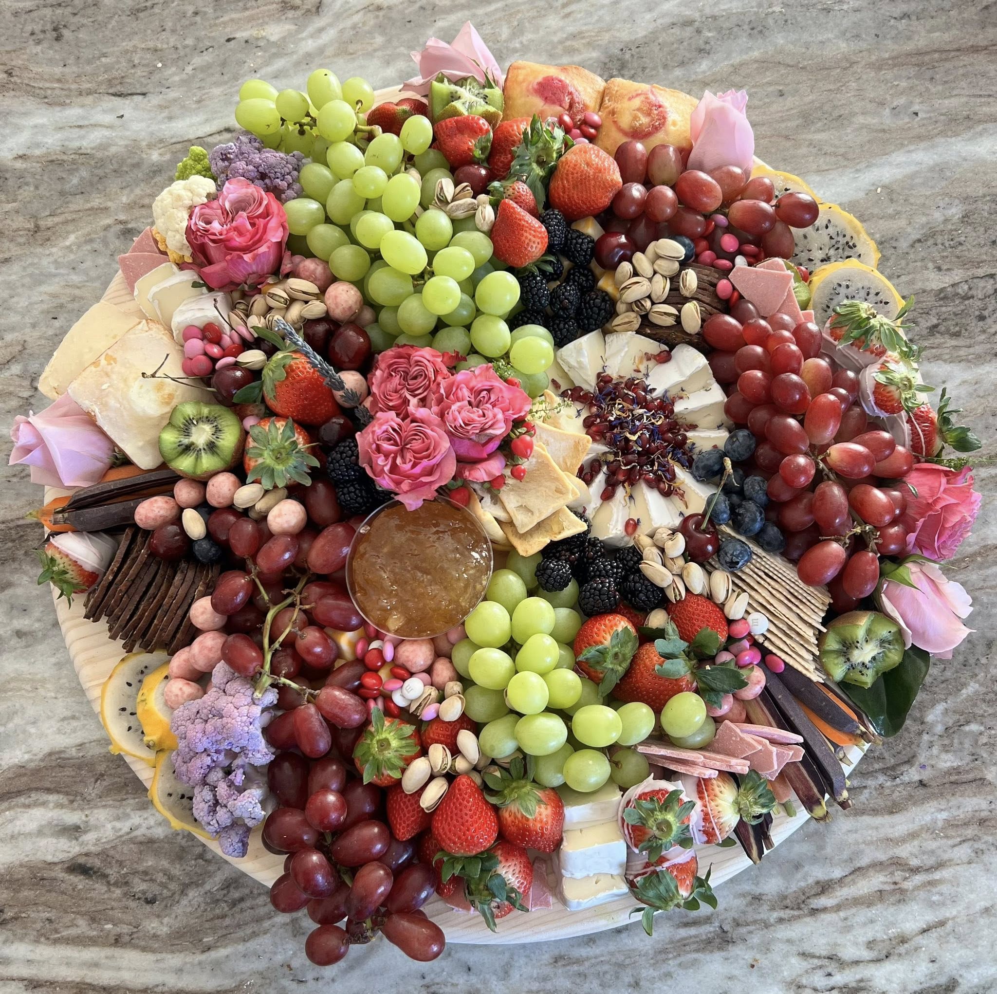 A round grazing board with brie, charcuterie roses, raspberries, and pink garden roses